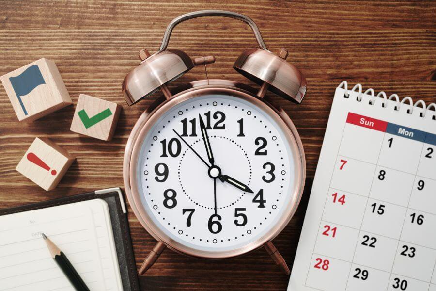 Image of a clock, a calendar and a notebook and pencil on a desk
